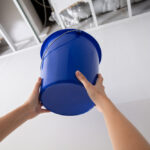 woman holding bucket under the leaking sewer pipe